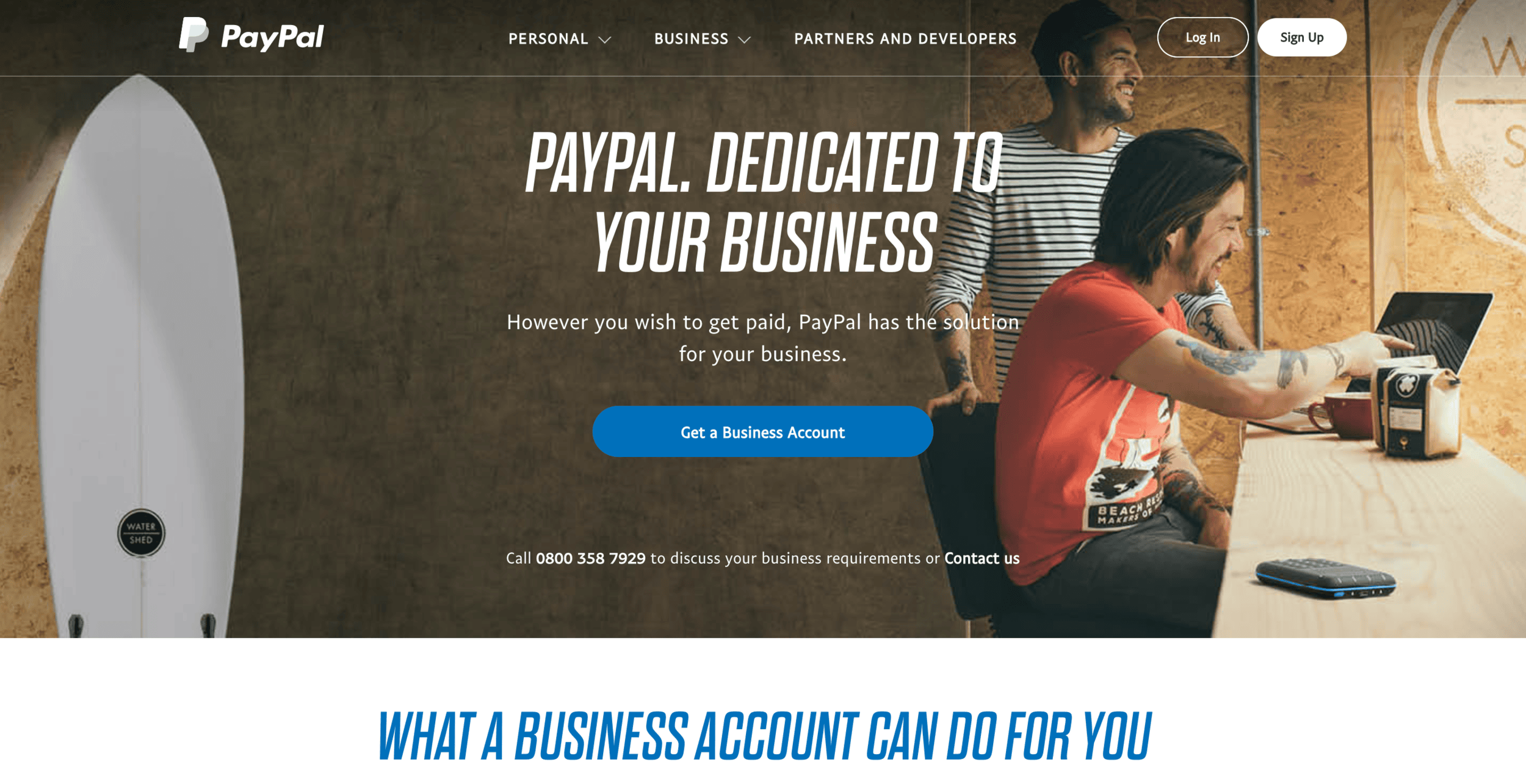 PayPal business homepage showing two entrepreneurs working on laptop with surfboard, promoting business payment solutions.