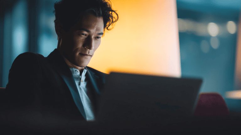 Man focused on laptop in dim light.