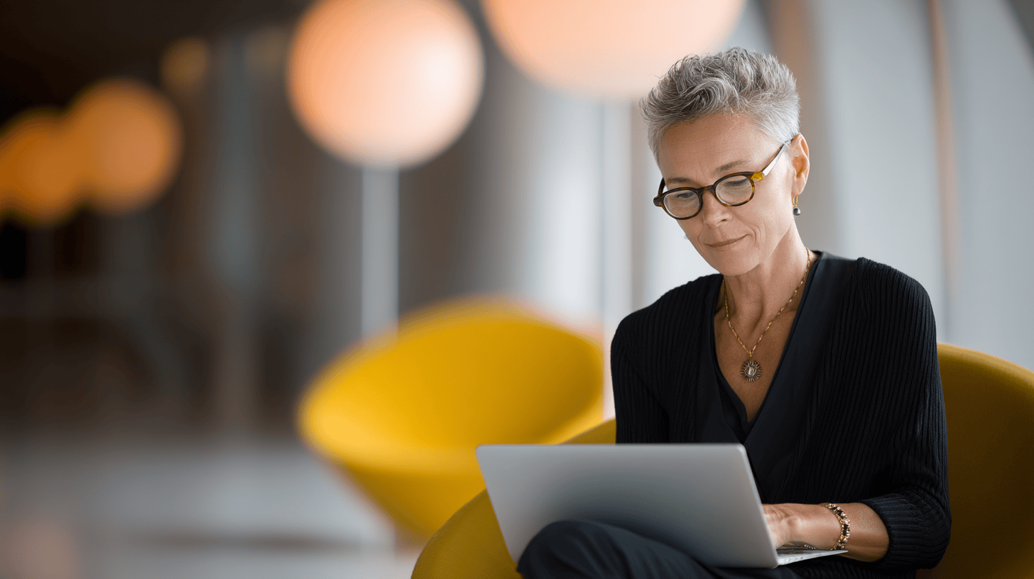 Elegant senior woman working on a laptop in a modern office space, representing professional business solutions and digital marketing.