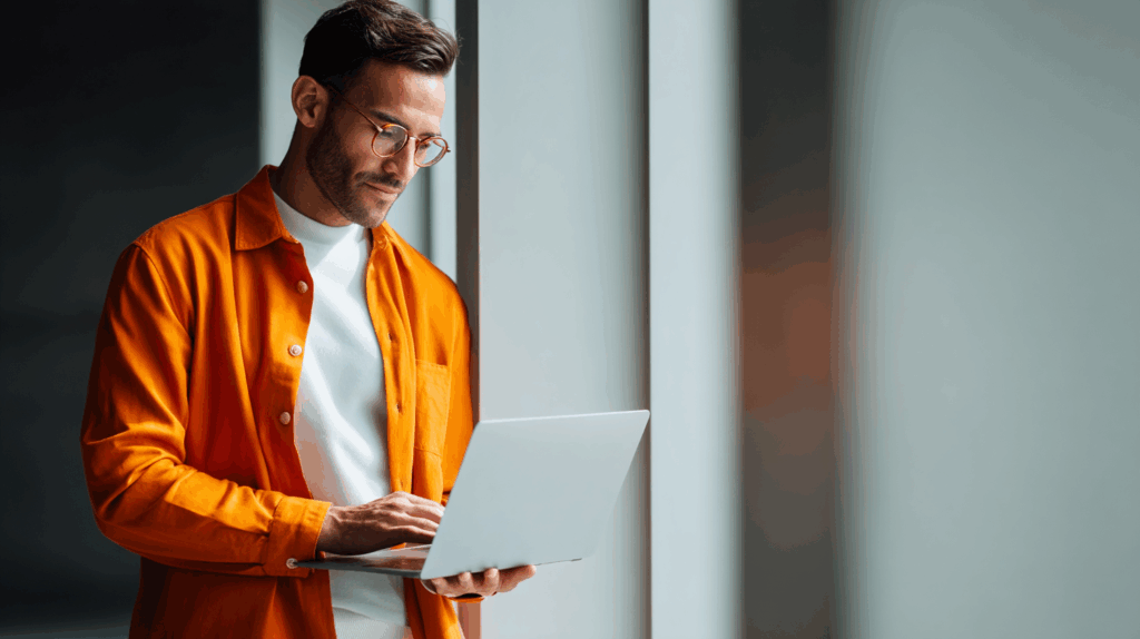 a man in an orange shirt and glasses holding a laptop