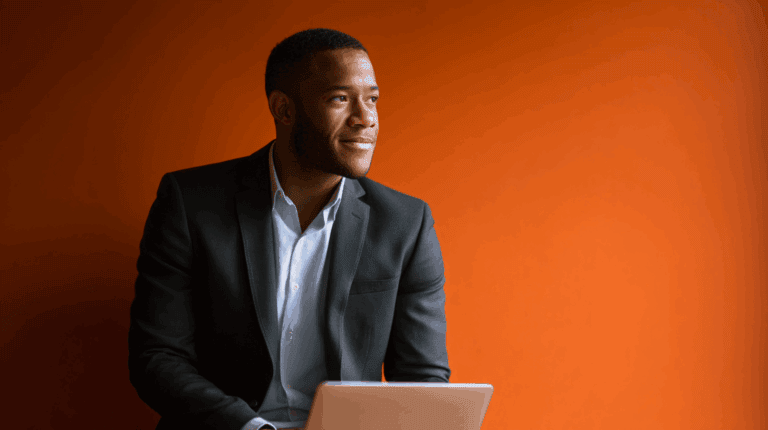 Man in suit with laptop against orange background.
