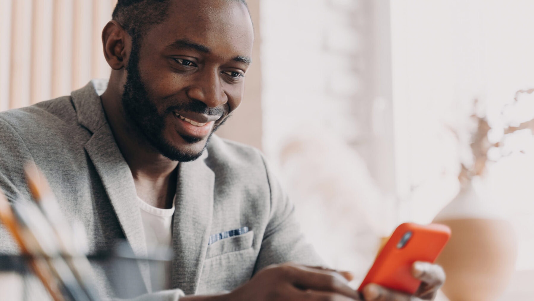 Handsome African American businessman, mobile use, chatting online, office desk, typing message, positive smile, distracted from work.