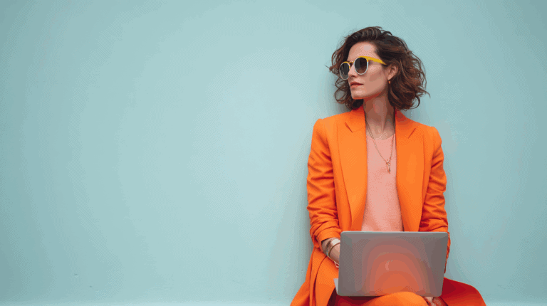 A woman in an orange suit sitting on a blue wall with a laptop.