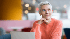 a woman with short hair wearing an orange sweater and earrings