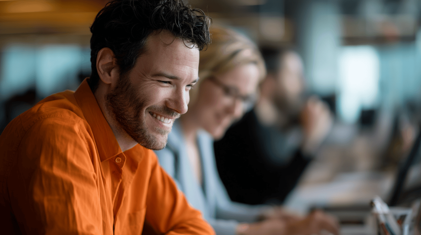 A professional man in an orange shirt working closely with teammates in a modern office, symbolizing the use of marketing automation to manage and optimize global campaign execution