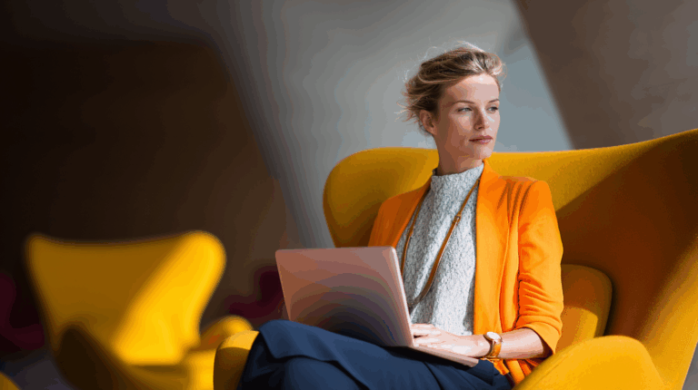 A woman sits comfortably in a bright yellow chair, working on a laptop. She wears an orange blazer over a light gray top, with her hair styled beautifully. The setting features soft lighting, creating a relaxed and modern atmosphere. The focus is on her thoughtful expression as she engages with her device.