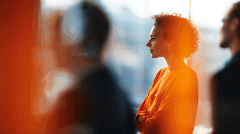 A woman with curly hair is captured in profile, wearing an orange sweater and earrings, standing thoughtfully with her arms crossed. The background features blurred figures and soft lighting, creating a warm ambiance. The scene suggests a moment of contemplation amidst a busy environment.