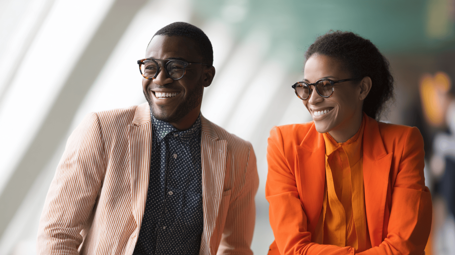 Two smiling individuals in fashionable outfits, one in a striped blazer and the other in an orange suit, against a bright background.