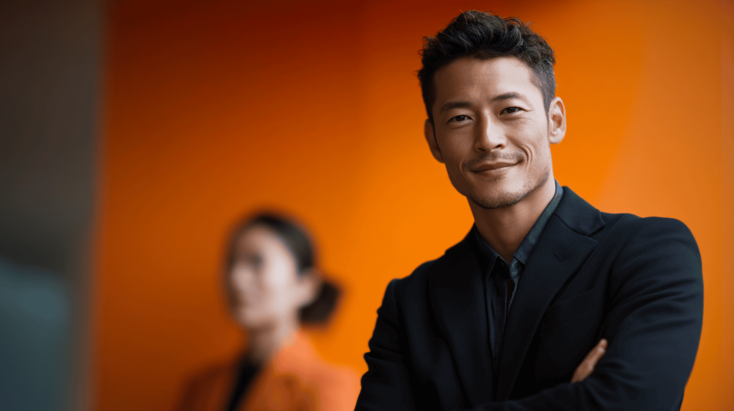 A confidently smiling man in a black suit stands in front of an orange background, while a blurred woman is visible behind him.