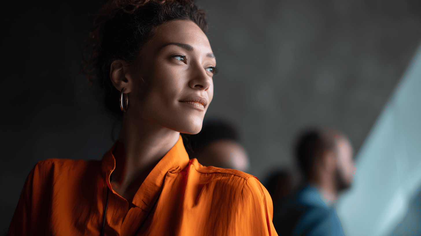 A woman in an orange shirt looks thoughtfully to the side, with blurry figures in the background.