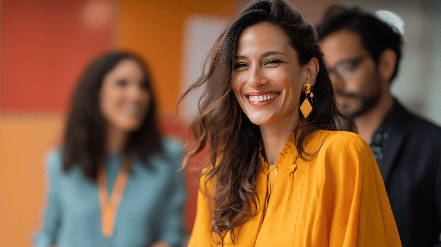 A woman in a bright yellow top smiles, with blurred figures in teal and black behind her, set against a colorful background.