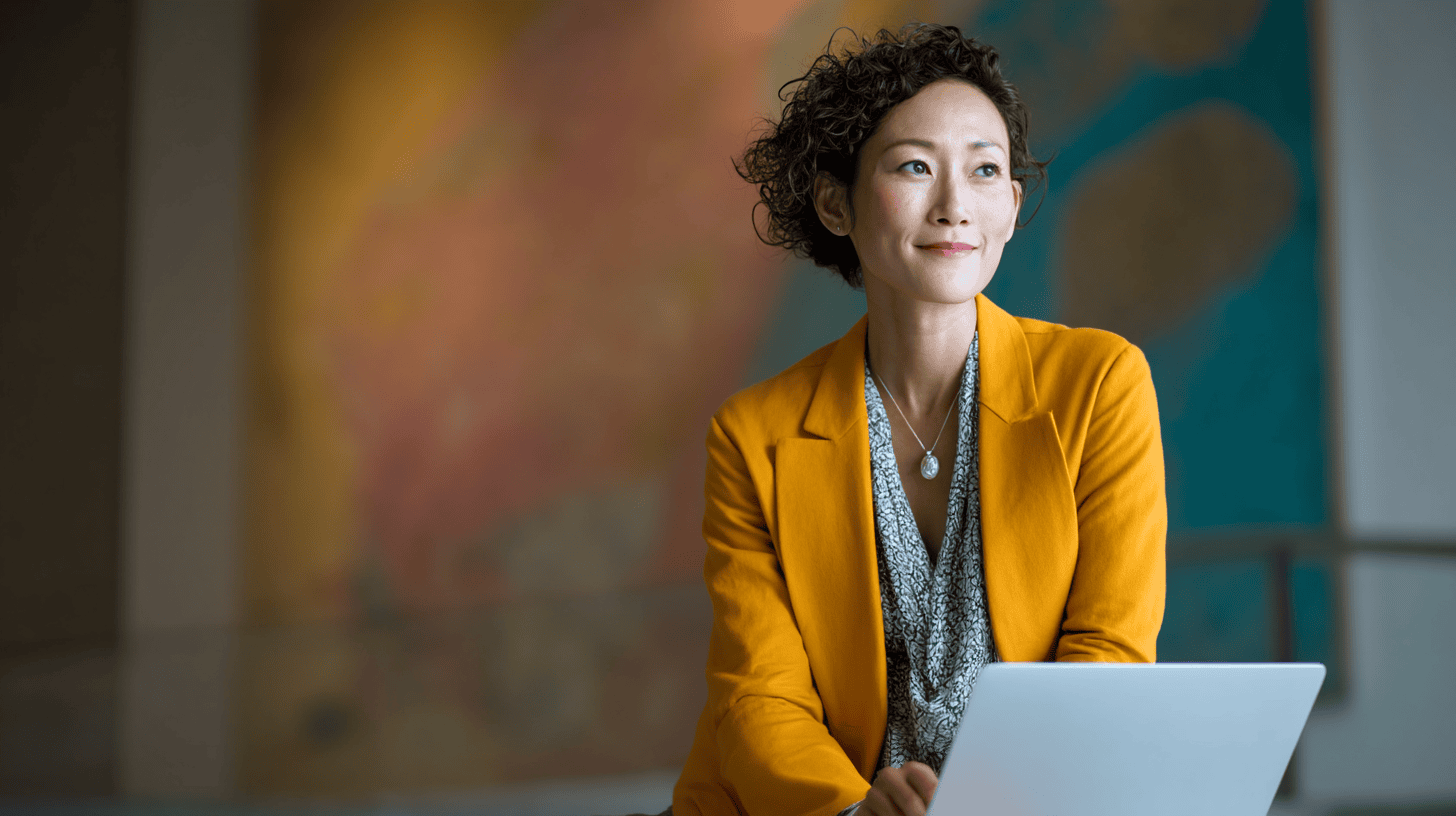 A woman in an orange blazer sits with a laptop, smiling, against a colorful abstract background.