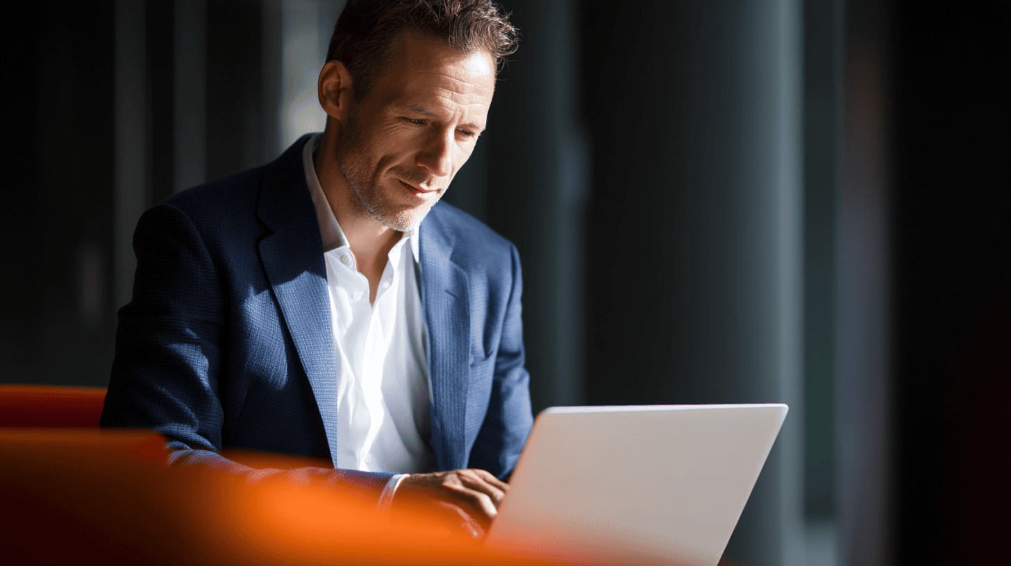 Business professional in a blazer focused on a laptop, seated in a modern environment with soft lighting.