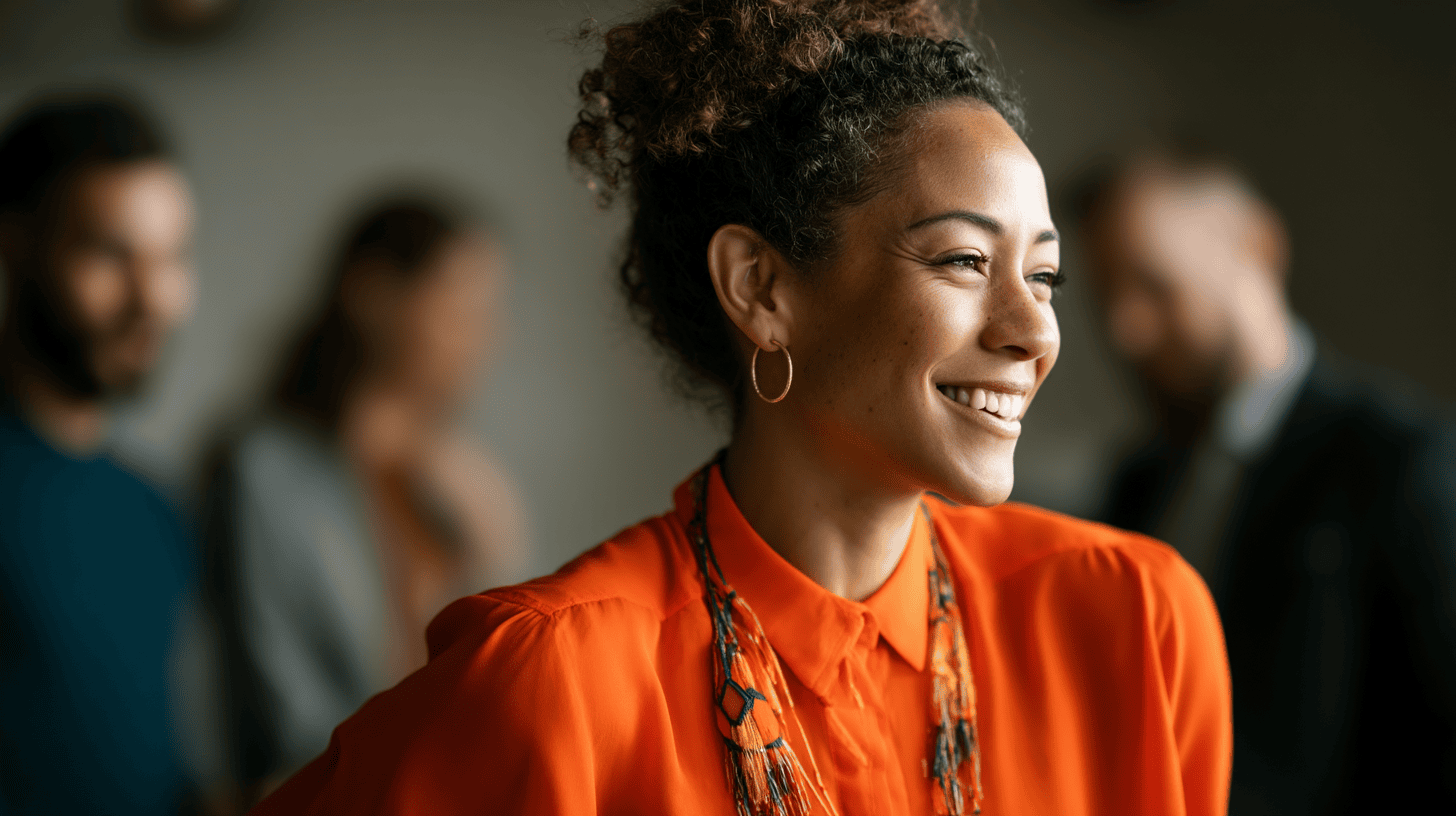 A woman in an orange blouse smiles, with blurred figures in the background, creating a warm, engaging atmosphere.
