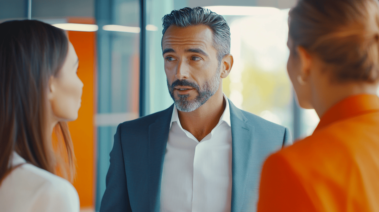 Three business professionals engaged in conversation in a modern office setting with bright colors and natural light.
