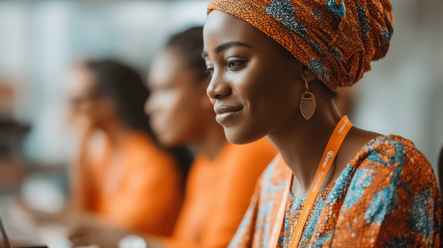 A woman in an orange and blue patterned outfit, wearing earrings, smiles while seated with others in a meeting.