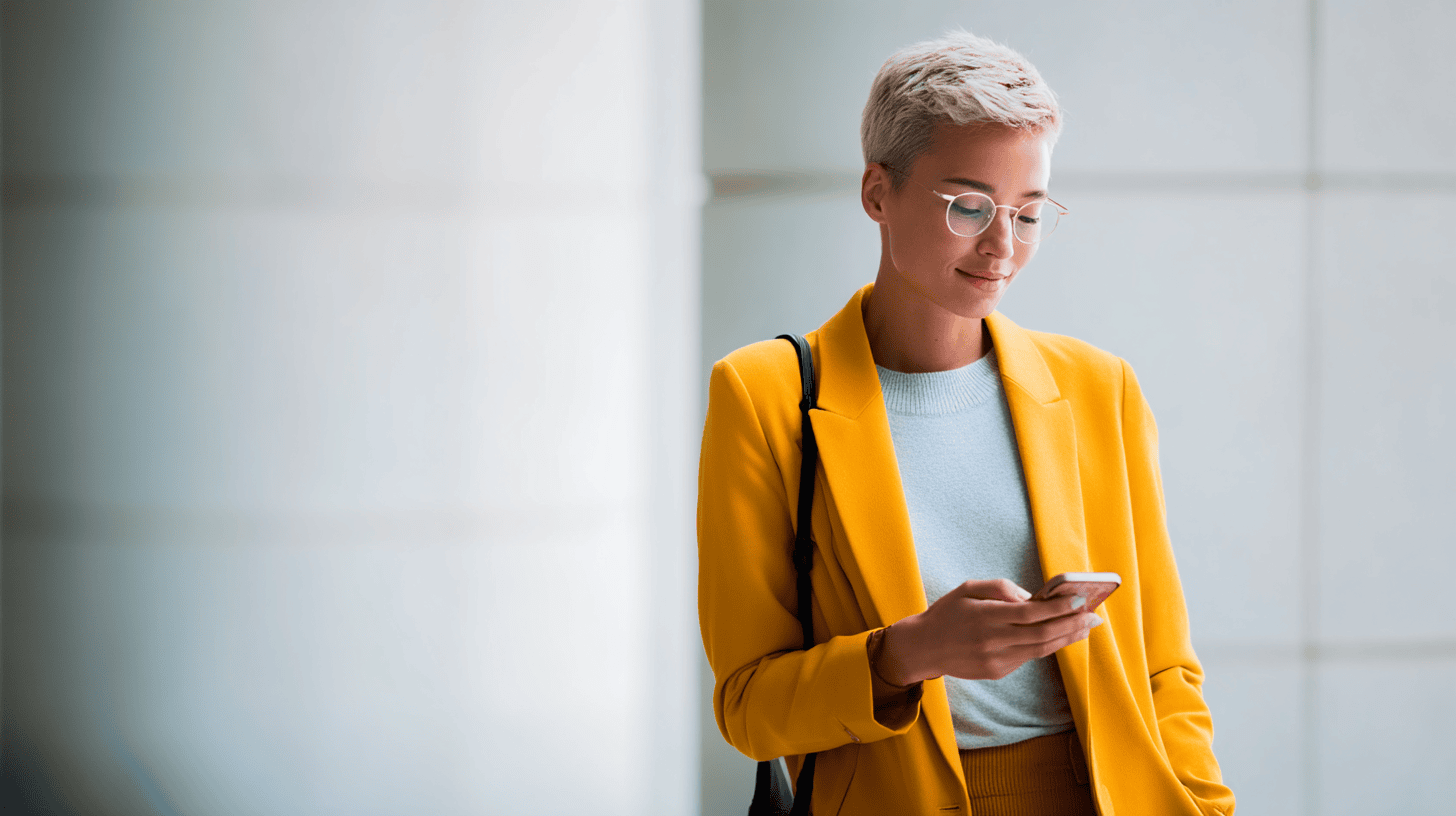 A woman in a bright yellow suit checks her phone, standing against a light-colored background.