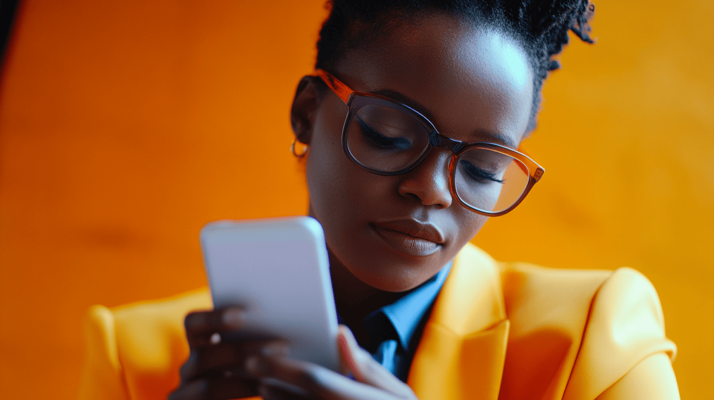 A woman in an orange blazer uses a smartphone, with a blurred orange background and her glasses framing a focused expression.