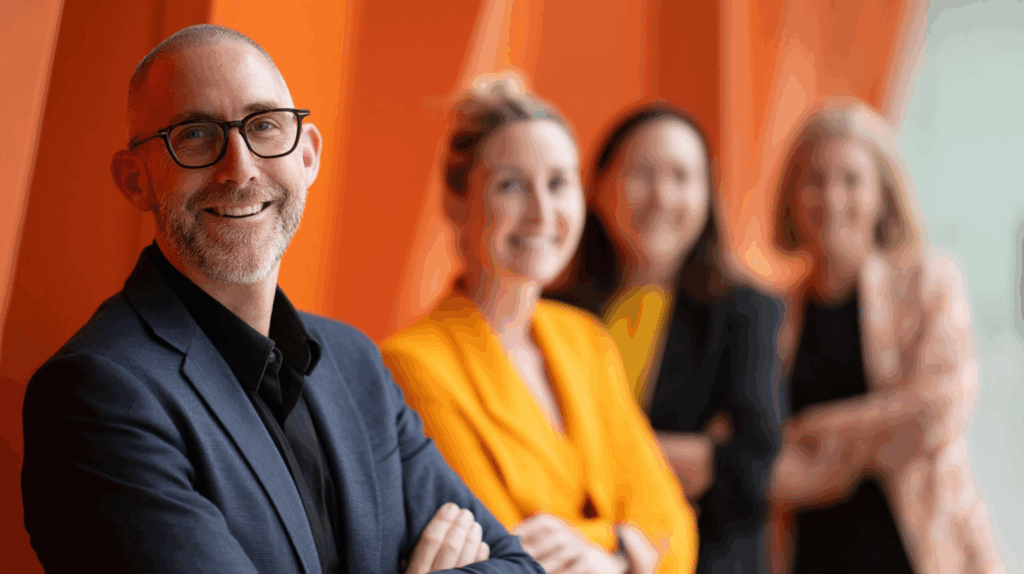 A group of business people standing in front of an orange wall.