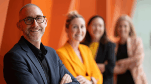 A group of business people standing in front of an orange wall.