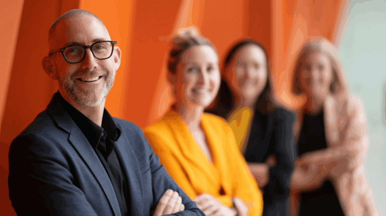 A group of business people standing in front of an orange wall.